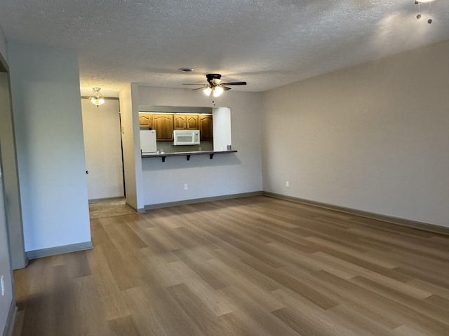 unfurnished living room with a textured ceiling, ceiling fan, baseboards, and light wood-type flooring