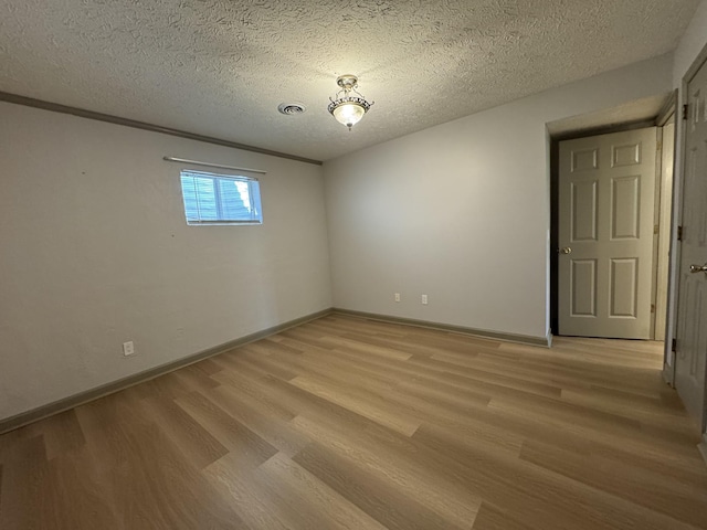 empty room with light wood-style floors, baseboards, a textured ceiling, and visible vents