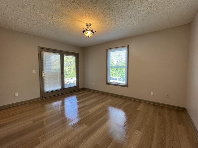 empty room with a textured ceiling, baseboards, and wood finished floors