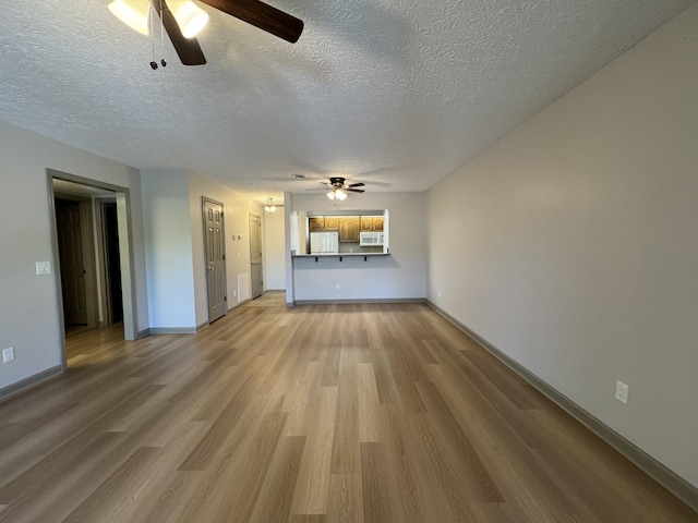 unfurnished living room with light wood-style floors, baseboards, ceiling fan, and a textured ceiling