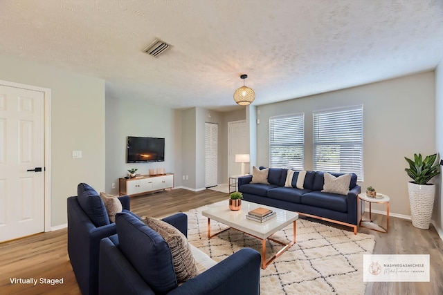 living area featuring visible vents, a textured ceiling, baseboards, and wood finished floors
