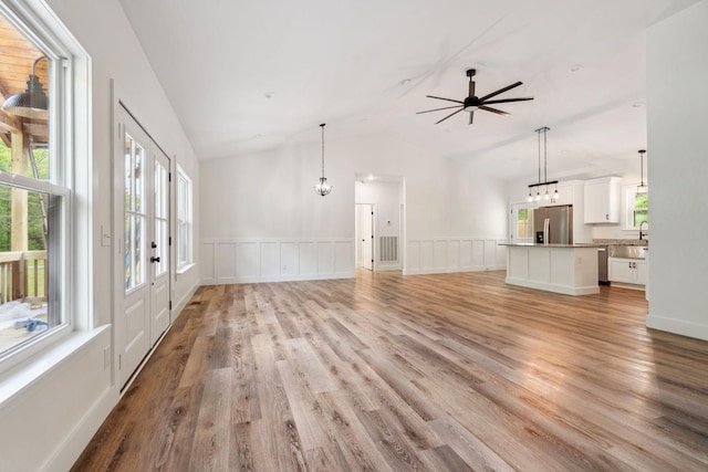 unfurnished living room featuring light wood-style floors, a wainscoted wall, ceiling fan with notable chandelier, and lofted ceiling