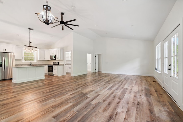 unfurnished living room with a notable chandelier, a sink, light wood-style floors, high vaulted ceiling, and baseboards