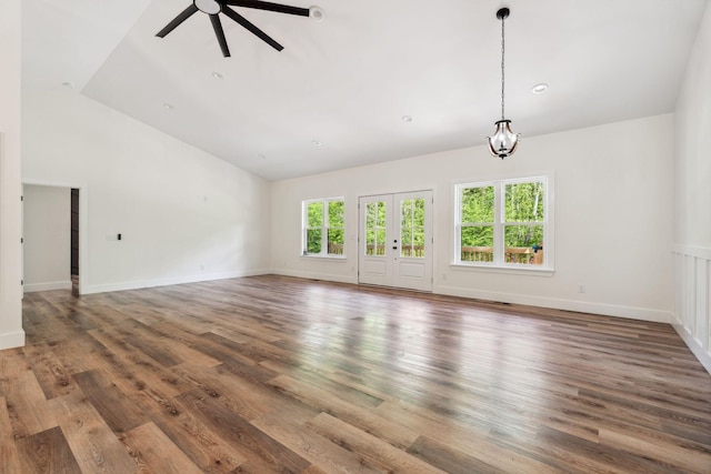 unfurnished living room with ceiling fan with notable chandelier, baseboards, vaulted ceiling, and wood finished floors