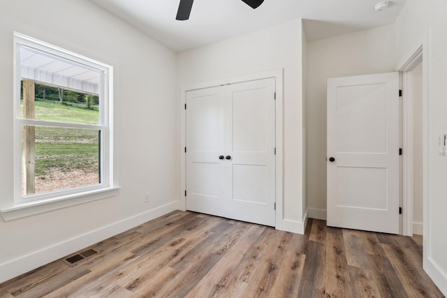 unfurnished bedroom with a ceiling fan, baseboards, wood finished floors, visible vents, and a closet