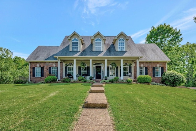 new england style home with brick siding, a shingled roof, a front lawn, and covered porch