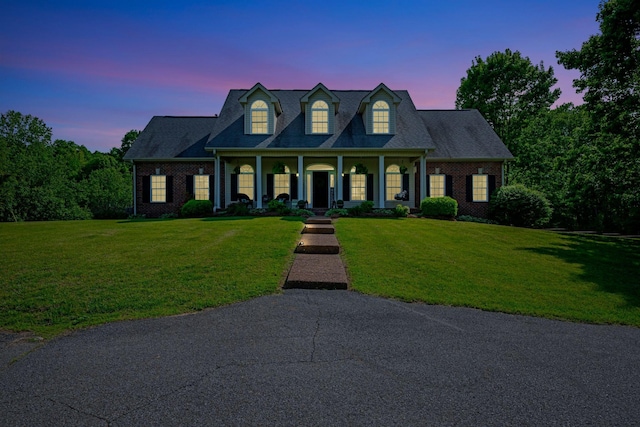 cape cod-style house featuring a yard, a porch, and brick siding