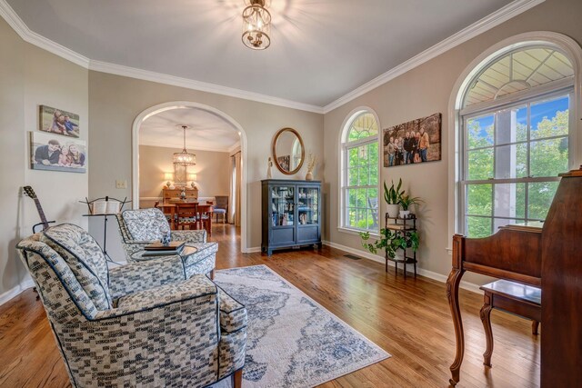 sitting room featuring crown molding, arched walkways, baseboards, and wood finished floors