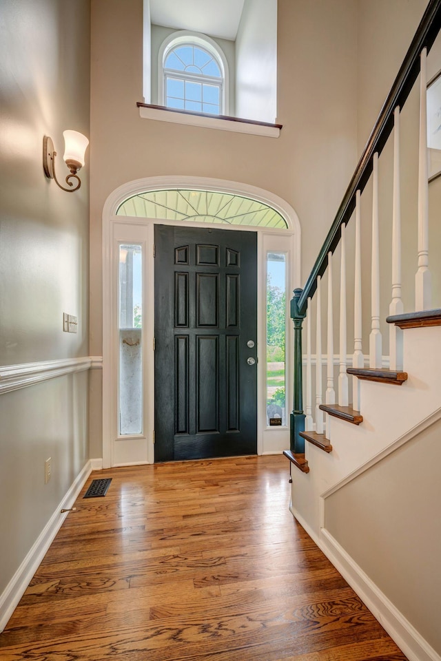 entryway featuring a high ceiling, stairs, baseboards, wood finished floors, and visible vents