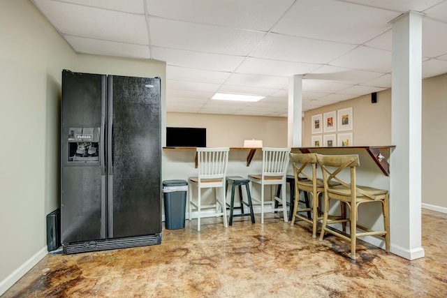 kitchen featuring baseboards, a paneled ceiling, and black fridge with ice dispenser