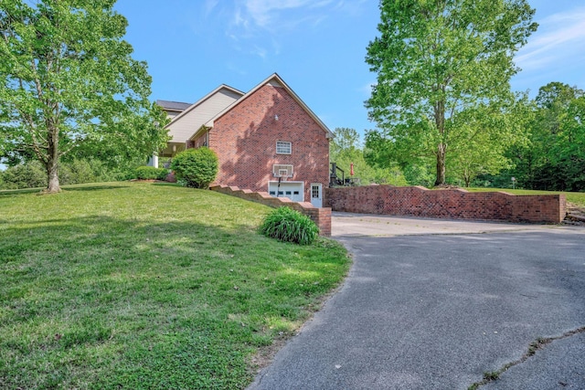 view of side of home featuring brick siding, a garage, a lawn, and driveway