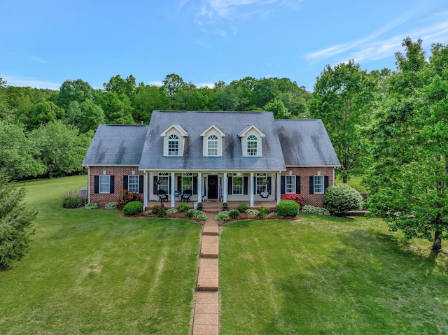 new england style home with a porch, a front lawn, and brick siding