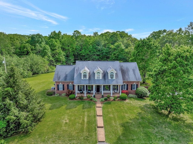 cape cod house with covered porch, brick siding, a view of trees, and a front yard