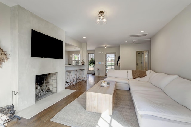 living room featuring recessed lighting, visible vents, a fireplace with raised hearth, and wood finished floors