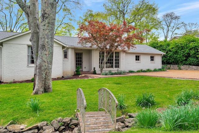 back of property featuring brick siding, a lawn, and roof with shingles