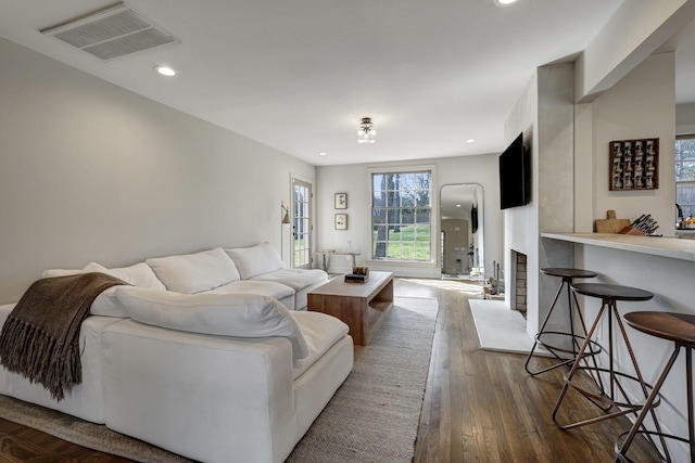 living area featuring a fireplace with raised hearth, visible vents, dark wood finished floors, and recessed lighting