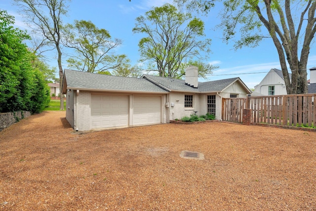 rear view of property featuring fence, a chimney, brick siding, a shingled roof, and an attached garage