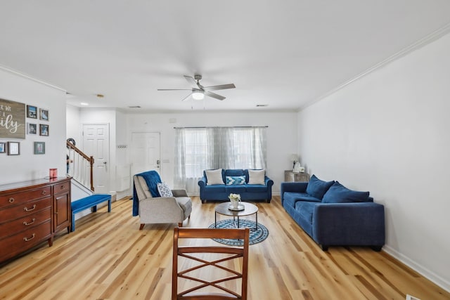 living area with crown molding, light wood-style floors, baseboards, ceiling fan, and stairway