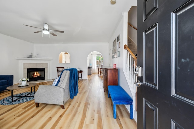 living area with a fireplace, ceiling fan, stairway, light wood-type flooring, and arched walkways