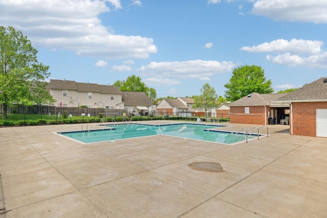 community pool with a patio, fence, and a residential view