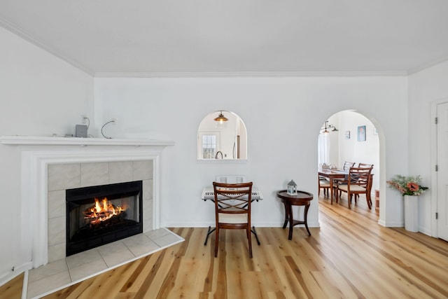 sitting room featuring ornamental molding, wood finished floors, a fireplace, baseboards, and arched walkways