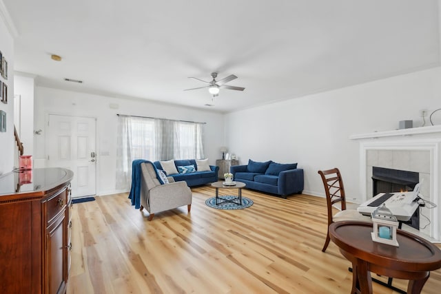 living area featuring ceiling fan, baseboards, light wood-type flooring, a tile fireplace, and visible vents