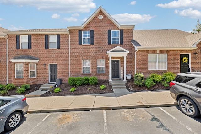 multi unit property with a shingled roof, uncovered parking, and brick siding