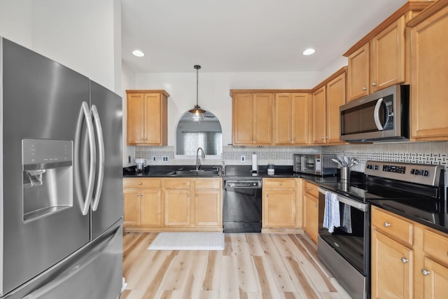 kitchen with dark countertops, appliances with stainless steel finishes, a sink, and tasteful backsplash