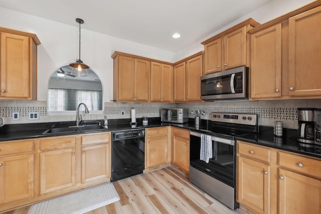 kitchen featuring stainless steel appliances, dark countertops, a sink, and light wood-type flooring