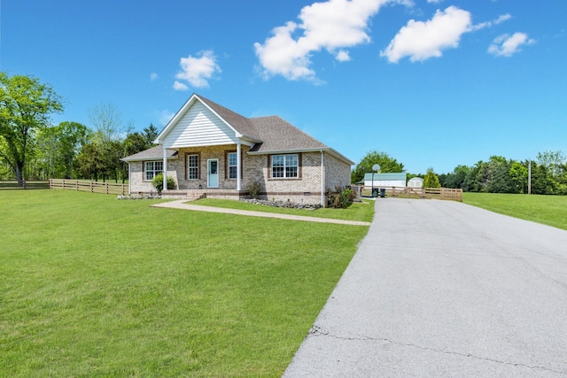view of front facade with brick siding, aphalt driveway, fence, and a front yard