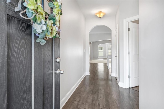 corridor with baseboards, arched walkways, and wood finished floors