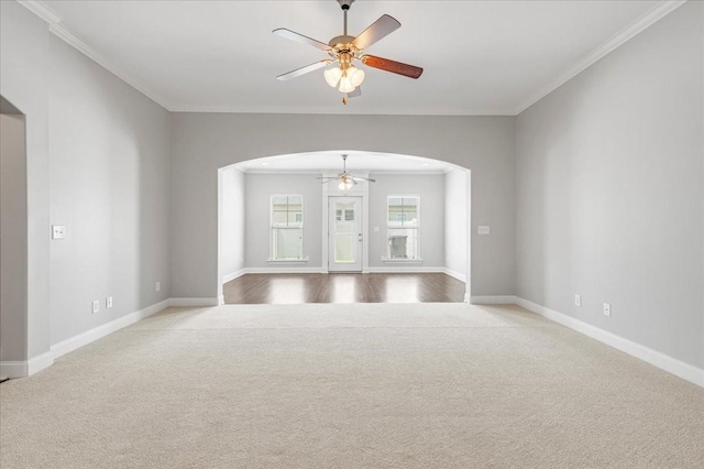 unfurnished room with carpet flooring, arched walkways, ceiling fan, and crown molding