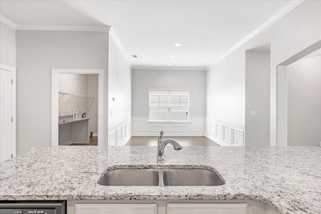 kitchen featuring crown molding, light stone countertops, a sink, and a wainscoted wall