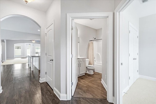 corridor with dark wood-style flooring, arched walkways, and baseboards