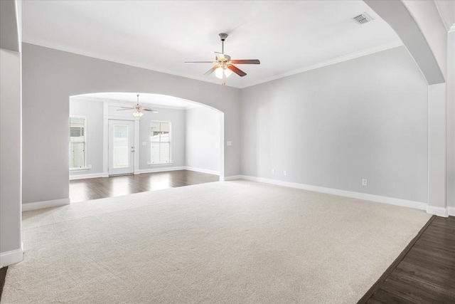 unfurnished living room with visible vents, a ceiling fan, crown molding, baseboards, and arched walkways