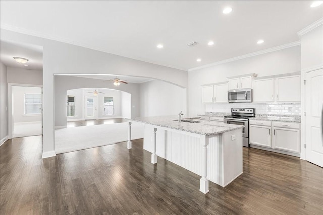 kitchen with open floor plan, ceiling fan, white cabinets, arched walkways, and stainless steel appliances