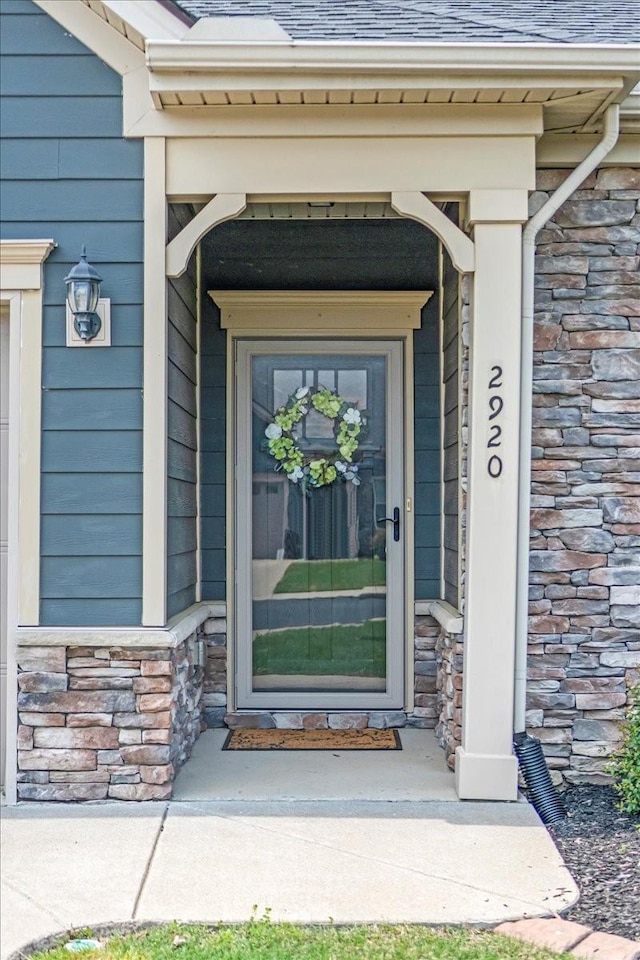 doorway to property featuring a shingled roof, a porch, and stone siding