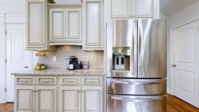 kitchen with cream cabinets, light stone counters, stainless steel fridge, decorative backsplash, and wood finished floors