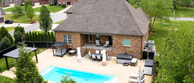 back of house with fence, roof with shingles, brick siding, a fenced in pool, and a patio