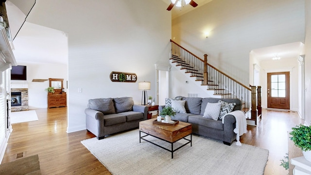 living area with visible vents, stairs, a towering ceiling, wood finished floors, and ceiling fan