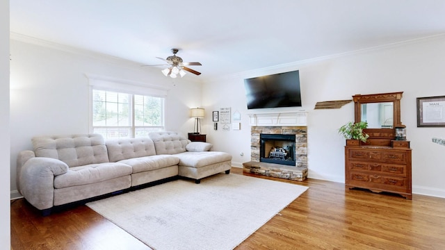 living room featuring ceiling fan, a fireplace, baseboards, light wood finished floors, and ornamental molding