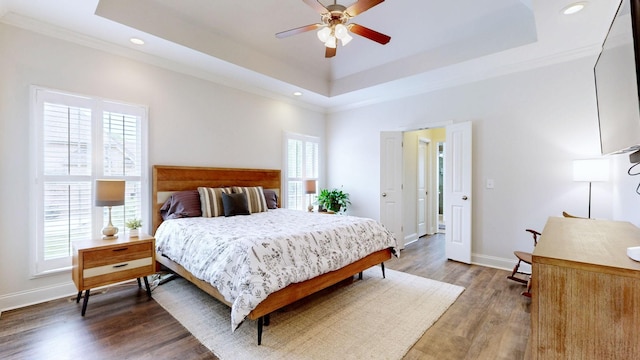 bedroom featuring ornamental molding, wood finished floors, baseboards, recessed lighting, and a tray ceiling
