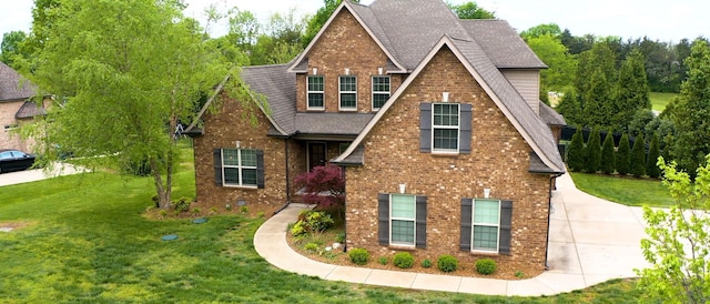 view of front of property with a shingled roof, a front lawn, and brick siding