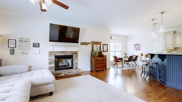 living area with ornamental molding, ceiling fan with notable chandelier, wood finished floors, and a fireplace