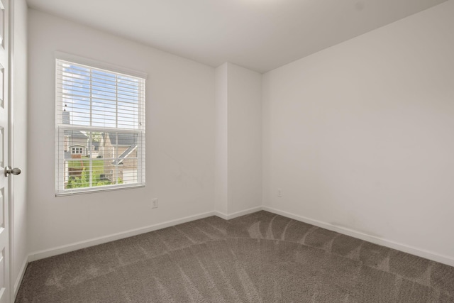 empty room with baseboards, a wealth of natural light, and dark colored carpet