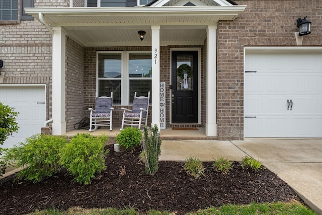 doorway to property with a porch, a garage, brick siding, and concrete driveway