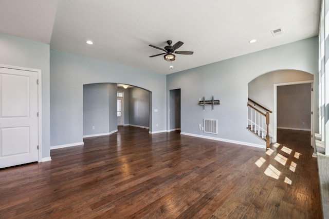 unfurnished living room with arched walkways, a ceiling fan, dark wood finished floors, and visible vents
