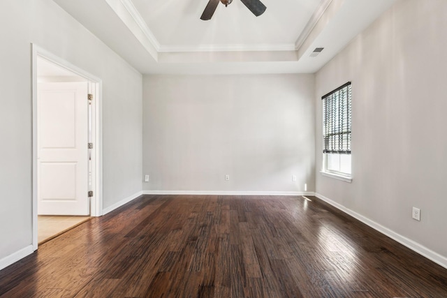 empty room with ornamental molding, dark wood-style flooring, ceiling fan, and a tray ceiling