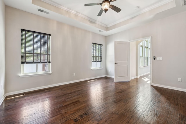 empty room featuring a ceiling fan, visible vents, crown molding, a raised ceiling, and dark wood-type flooring