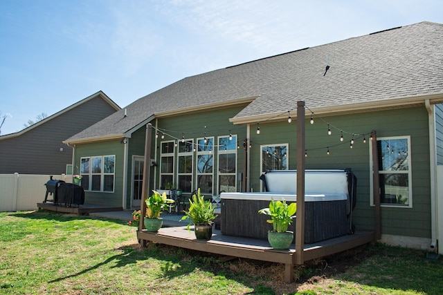 rear view of property with fence, a deck, a shingled roof, a hot tub, and a yard